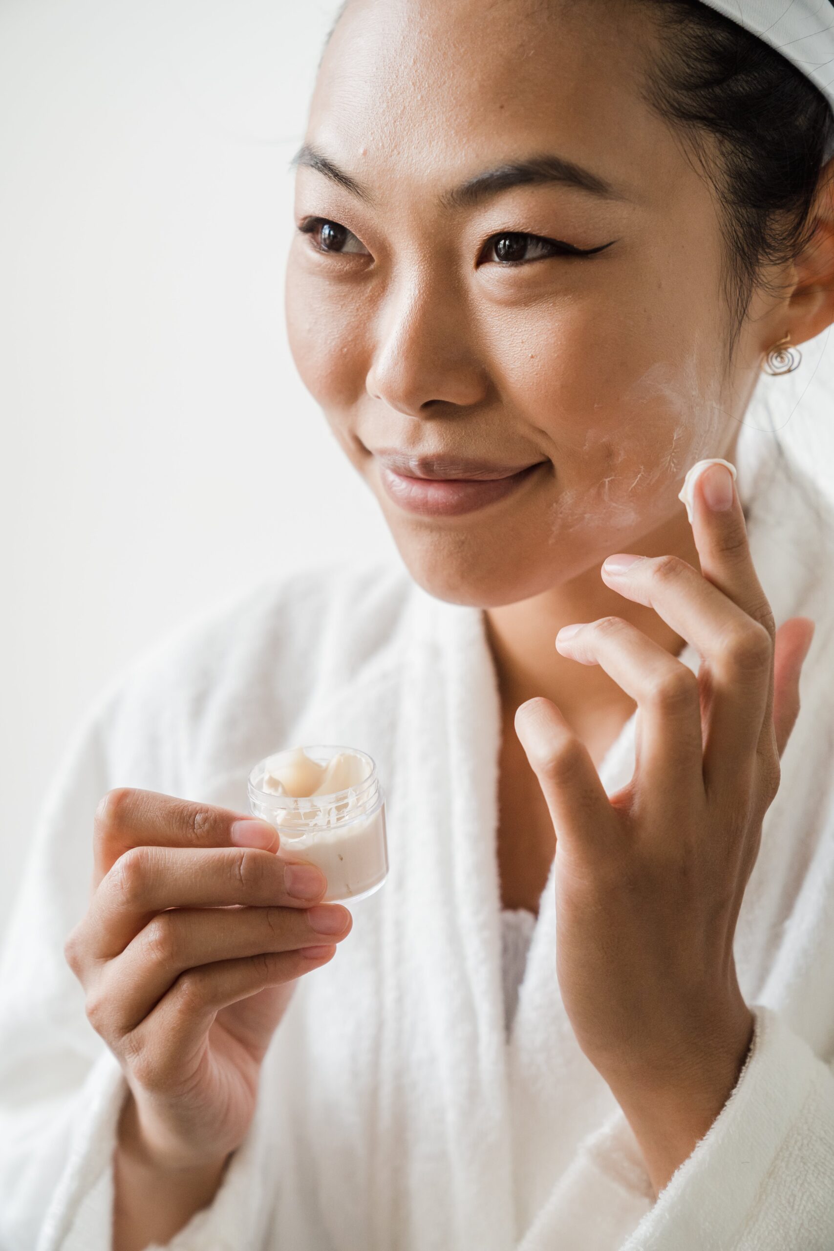 How to moisturize and revitalize dry, winter skin. Here is an image of a young Asian woman applying moisturizer cream to her face.