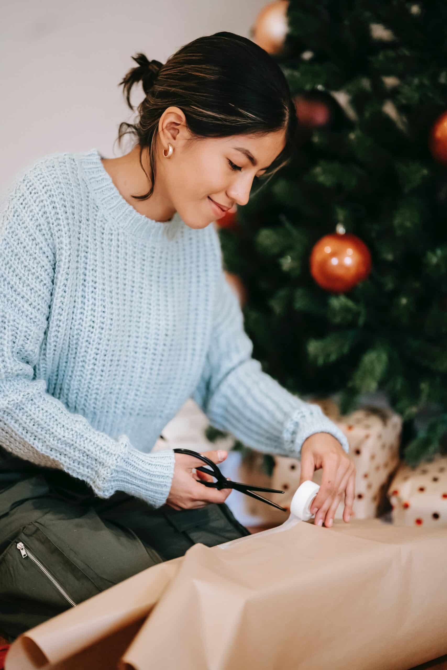 How to make the holidays more economical this season. The image is of a woman who is wrapping presents at home.